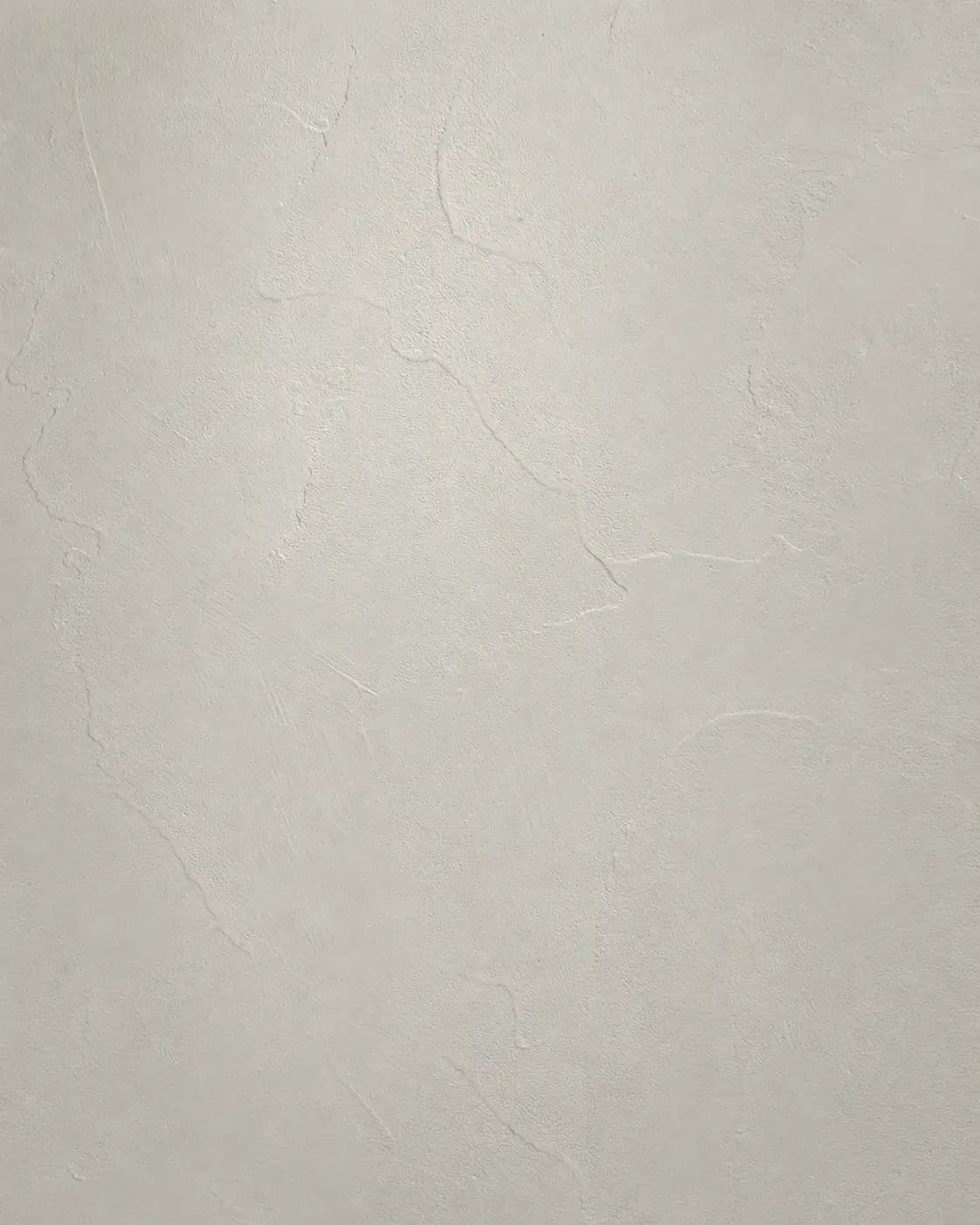 Close-up microcement texture sample in soft warm gray, showing the fine mineral surface and gentle trowel movement.