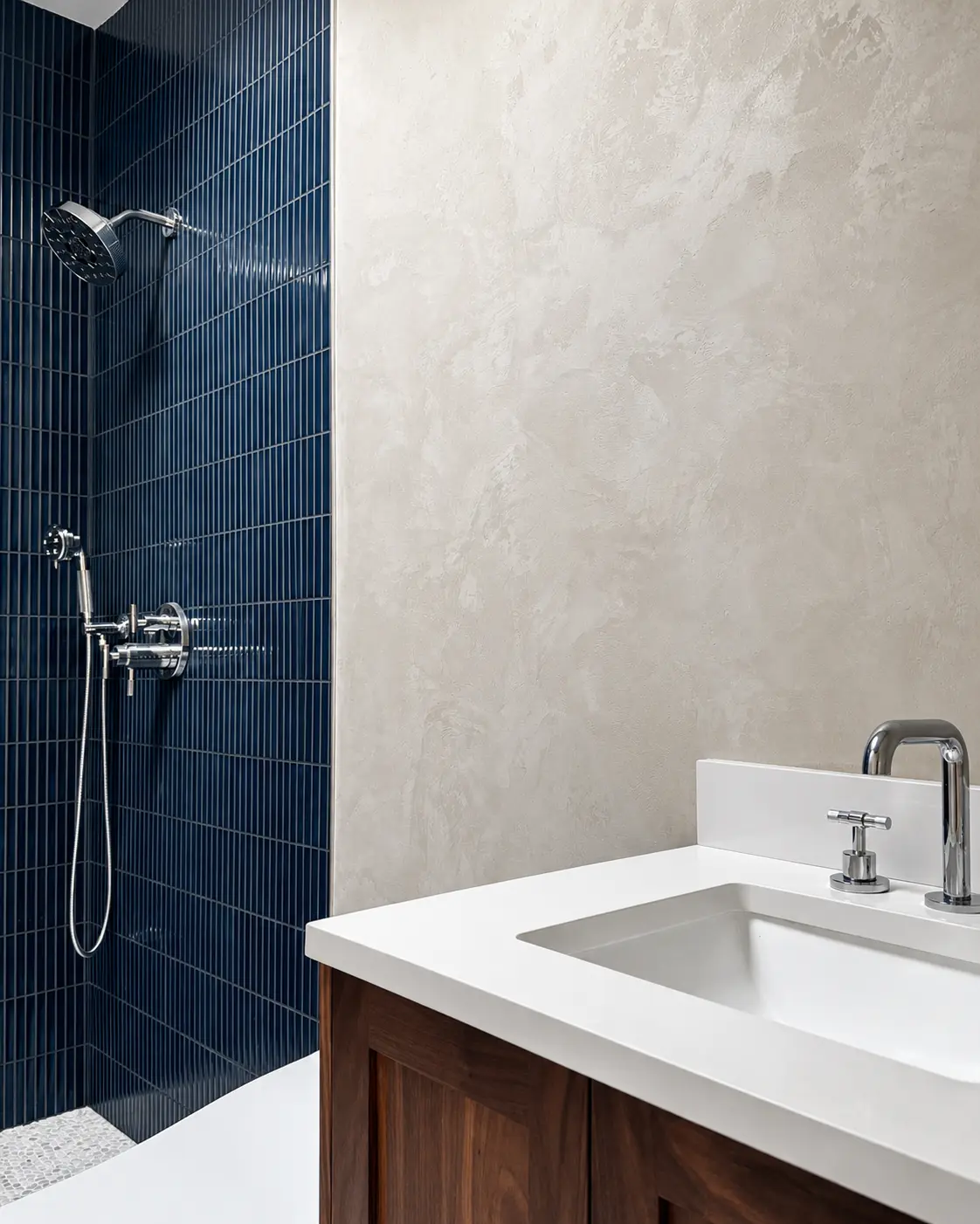 A light gray Venetian Marmorino bathroom wall beside a navy fluted-tile shower and a wood vanity, in a Santa Ana project.