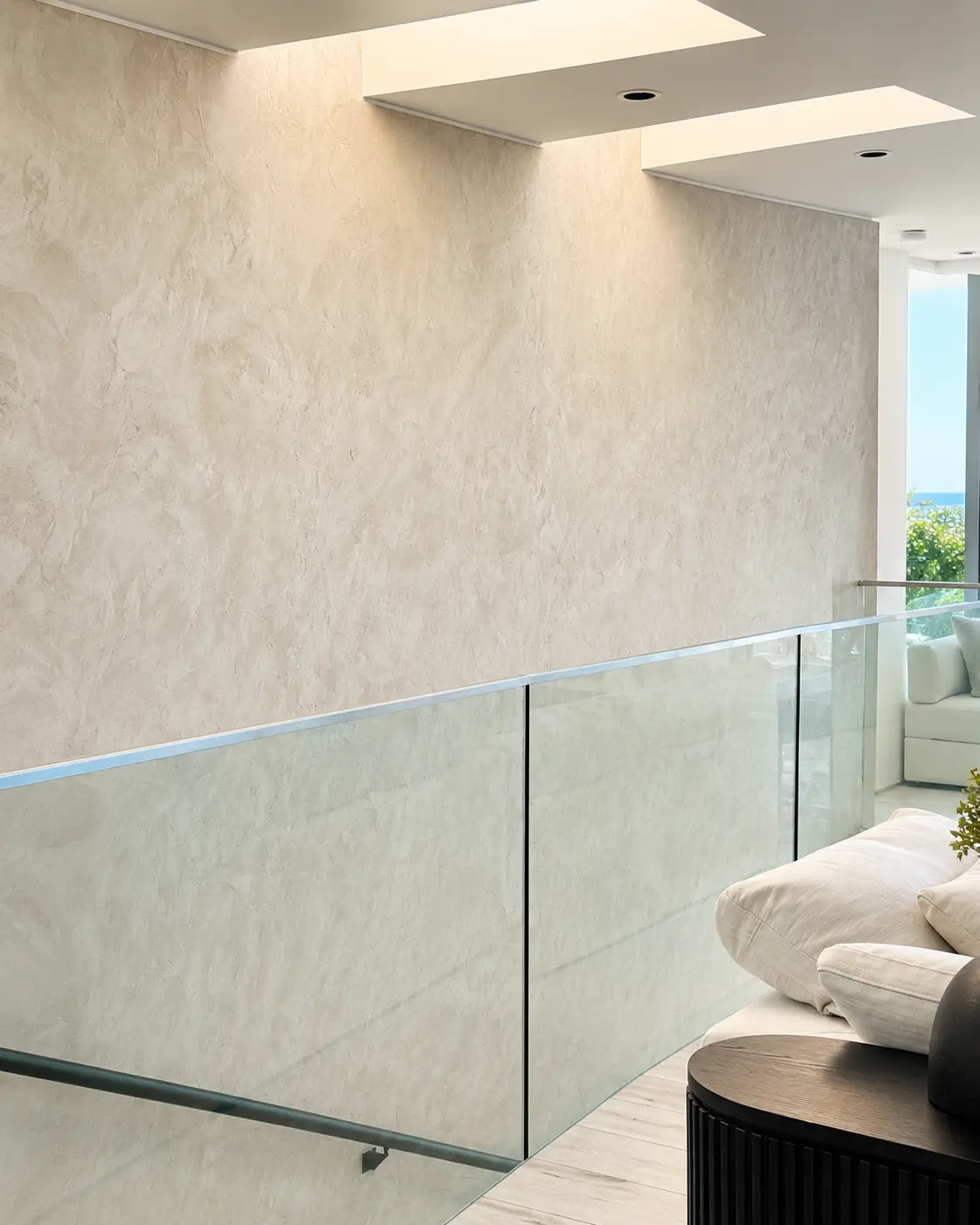 Light-catching Venetian plaster wall in a stair hall with a glass railing and ocean view, in a Laguna Beach project.