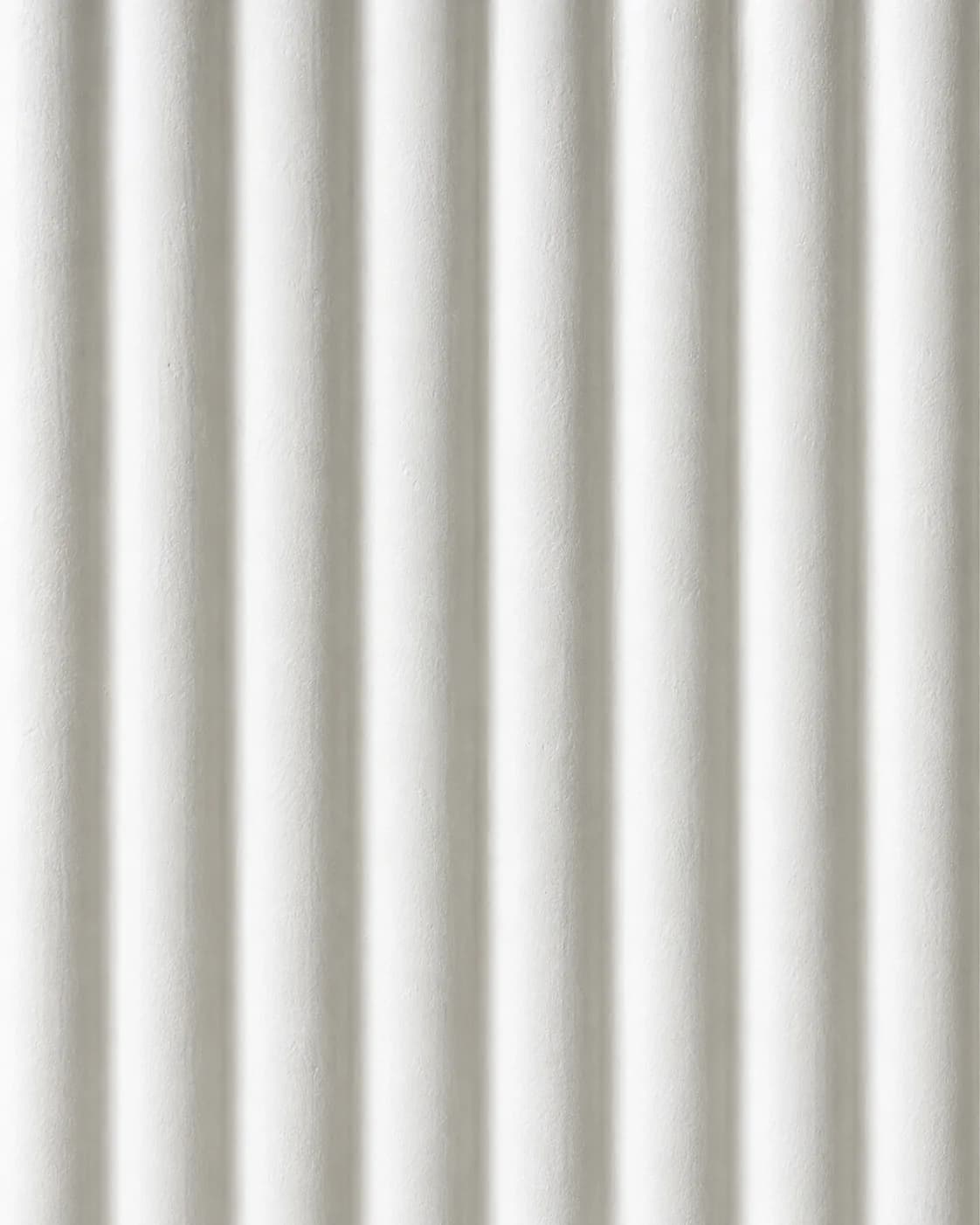Close-up of a fluted plaster surface showing the ridges and channels and the soft shadow movement between them.