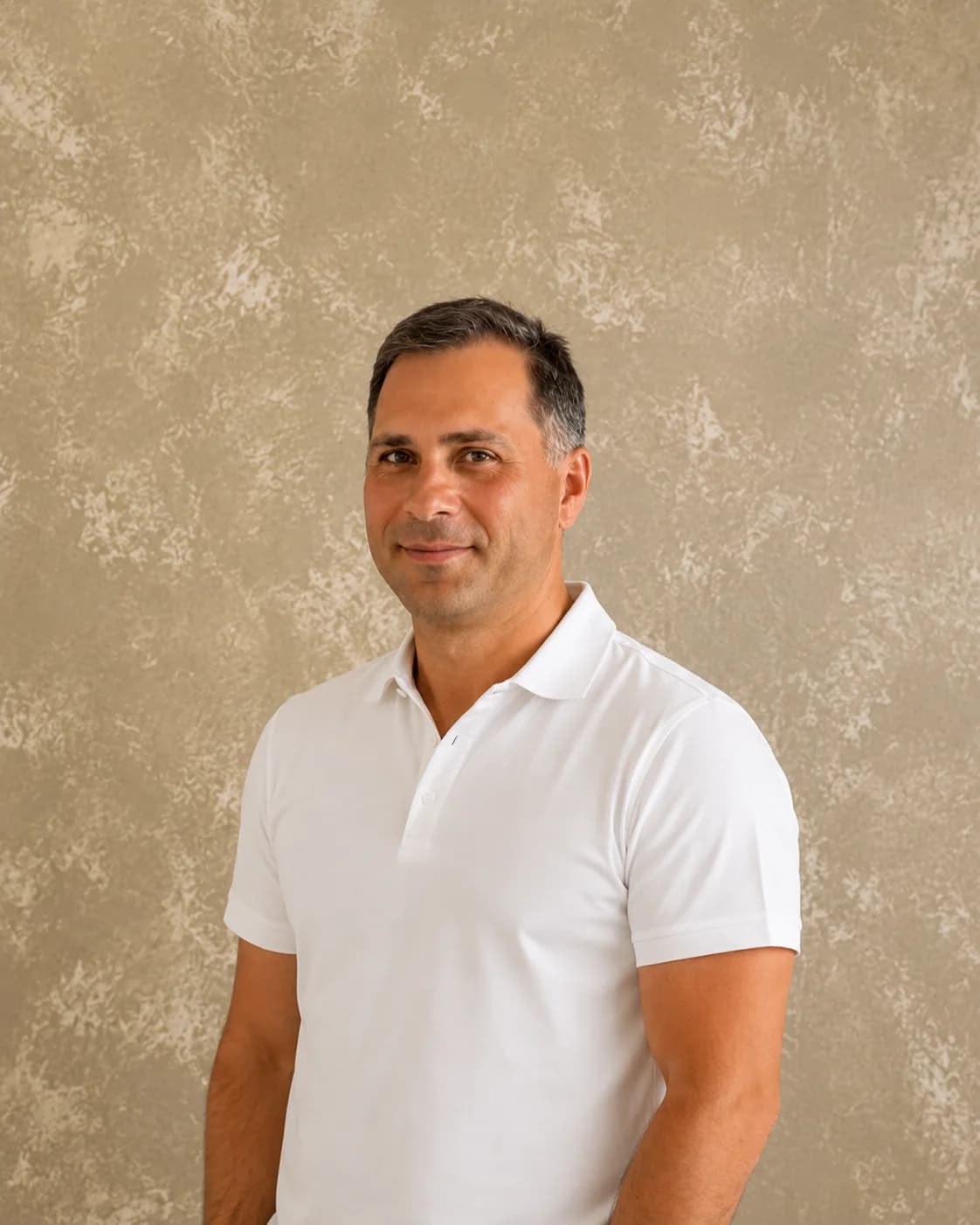 Igor Bakan, founder of SBK Group, in a white polo shirt against a textured plaster wall.