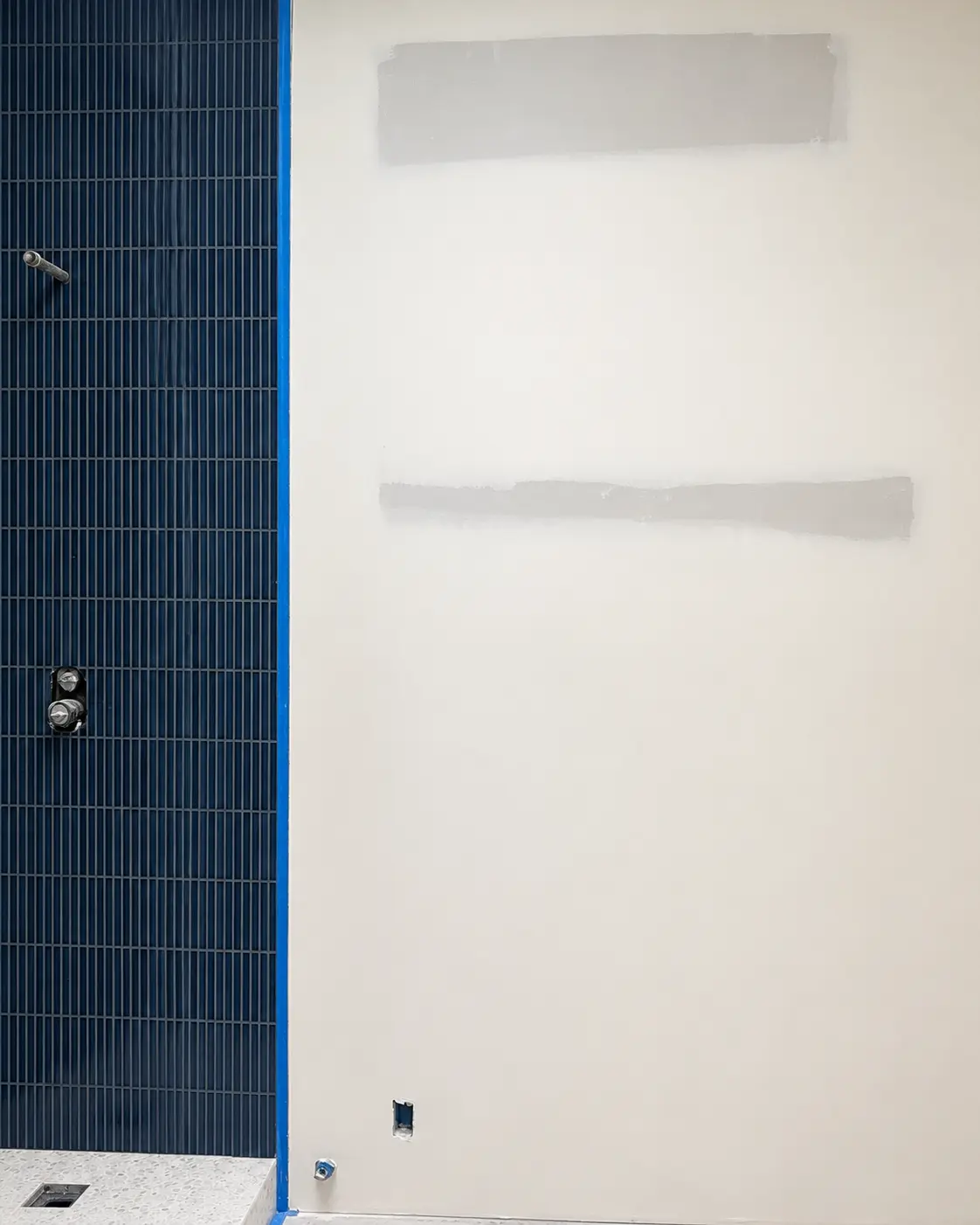 The shower-room wall before plastering, bare drywall beside the navy fluted-tile shower.