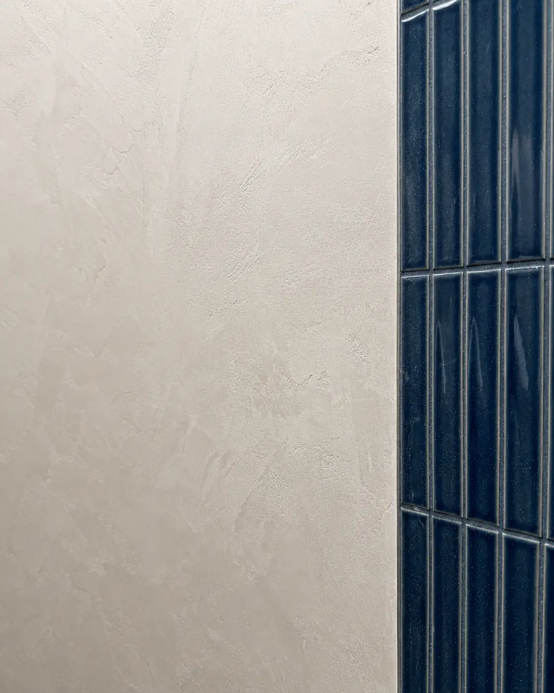 A close-up of the finished light gray Marmorino meeting the navy fluted-tile shower with a clean edge.