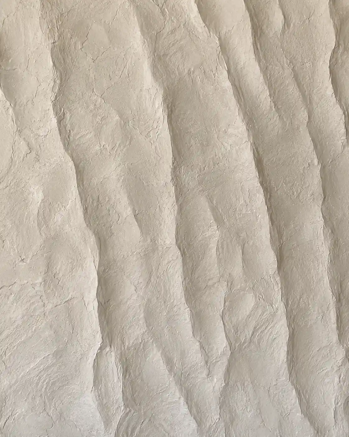 Real hand-applied sculpted rock stone-effect plaster sample in warm cream, with deep vertical hand-carved ridges and rugged relief.