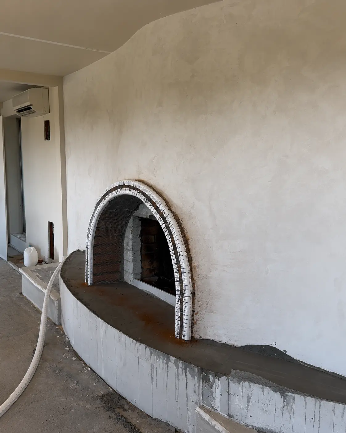 Arched fireplace opening reinforced with metal lath and corner bead, the curved hearth freshly rebuilt in cement before microcement.
