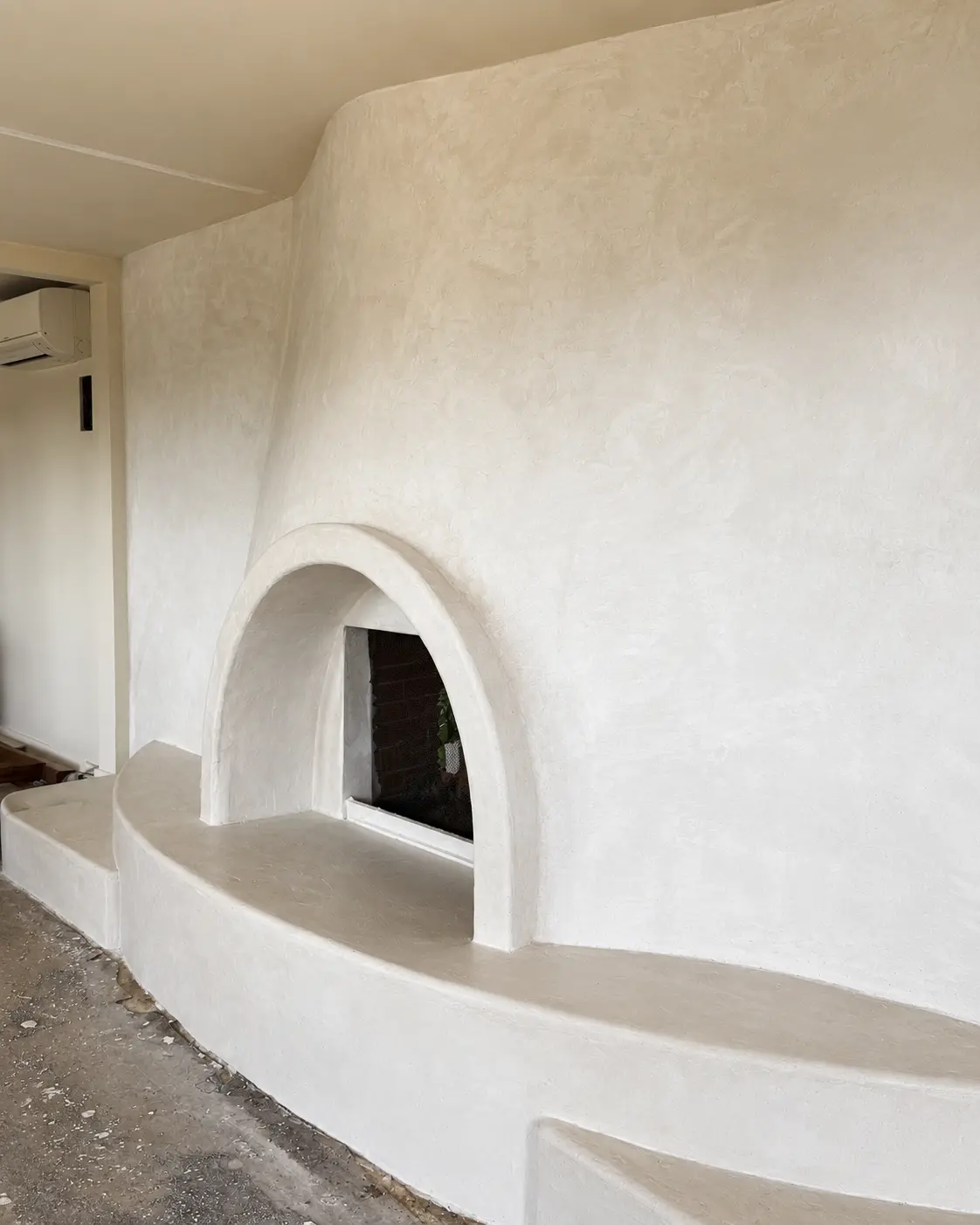 Fireplace after the first coat of microcement, a continuous light surface beginning to unify the arch and hearth.