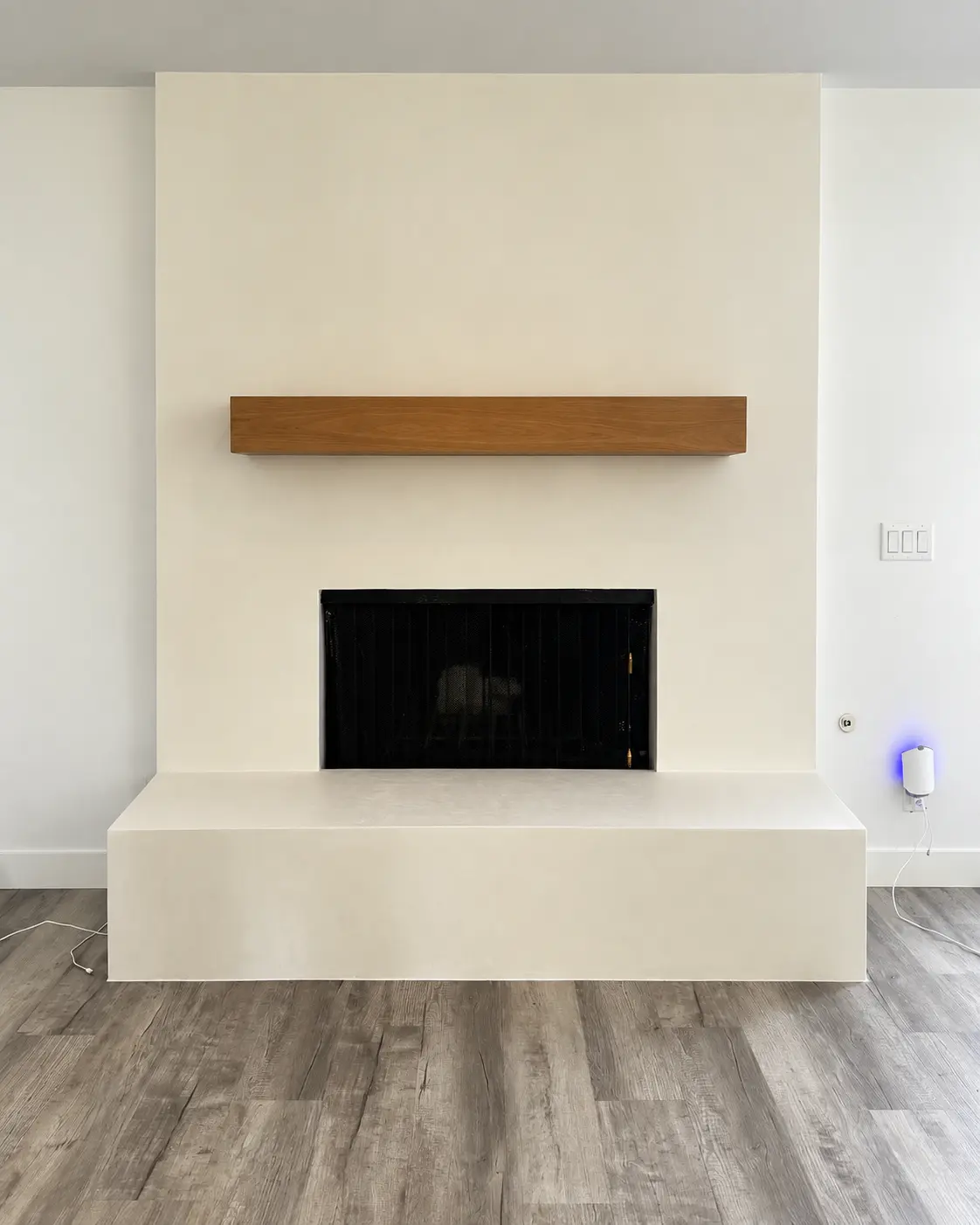 Completed Marmorino Tintoretto fireplace in MC-709 Pure White with a floating wood mantel in a Carlsbad living room.