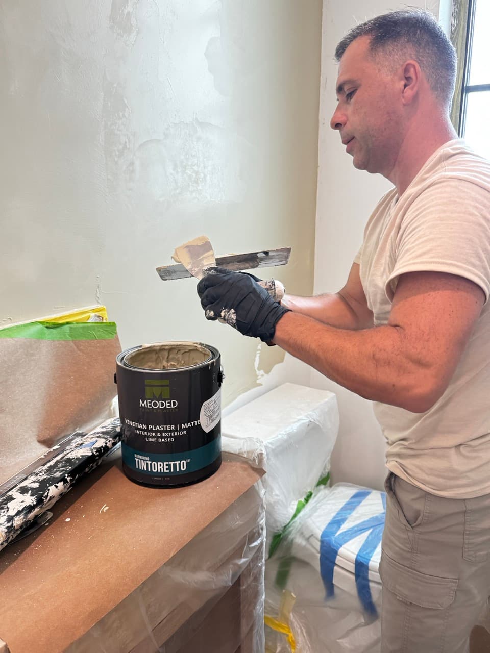 Specialist master loading a trowel from a Meoded Venetian plaster can in a masked powder room.