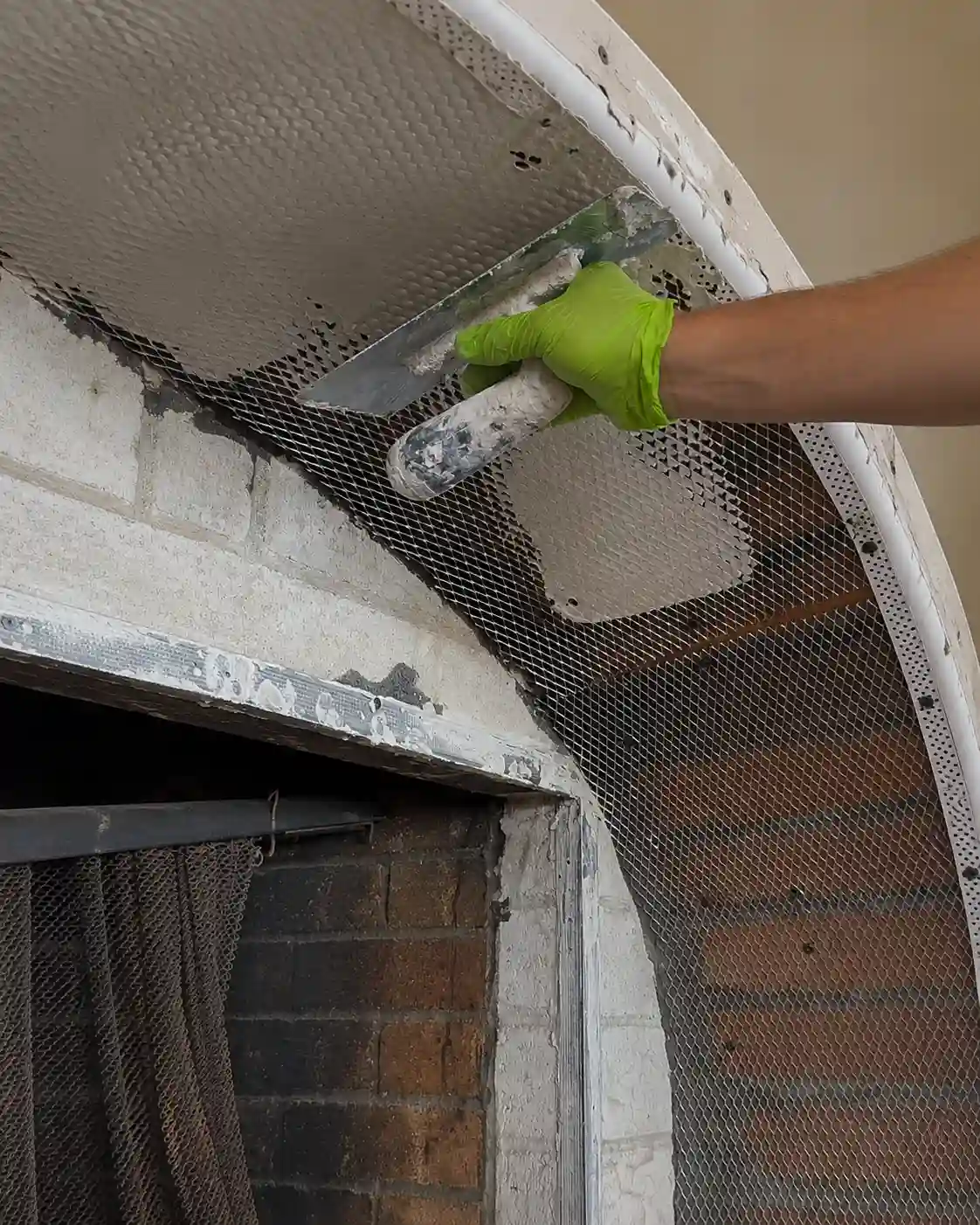 Specialist master troweling cement over metal lath inside the reinforced arch soffit, exposed firebox below.