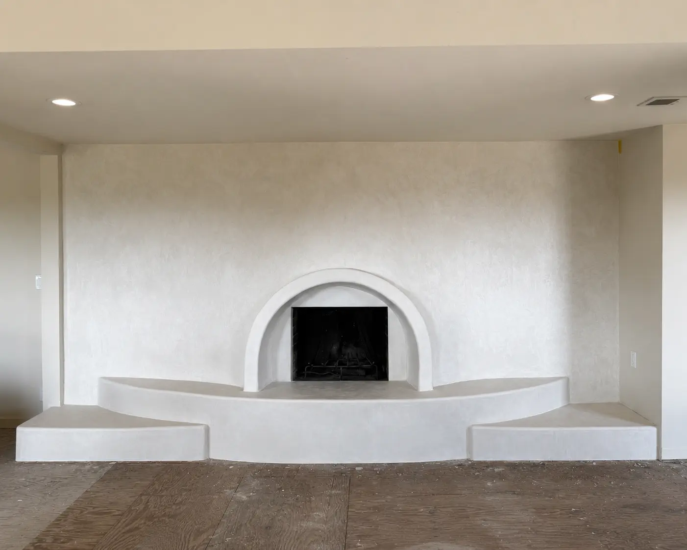 Finished White Dove microcement fireplace seen straight on, the arch and stepped hearth reading as one continuous light surface, San Diego.