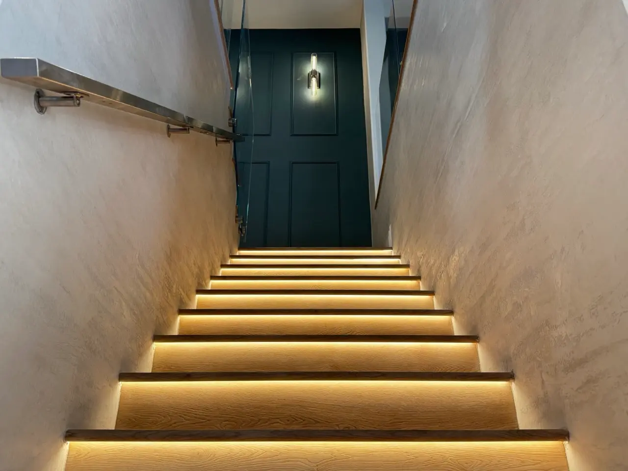 Completed stairwell finished in warm coffee Venetian plaster with a travertine effect, wood steps and integrated lighting, in Orange County.
