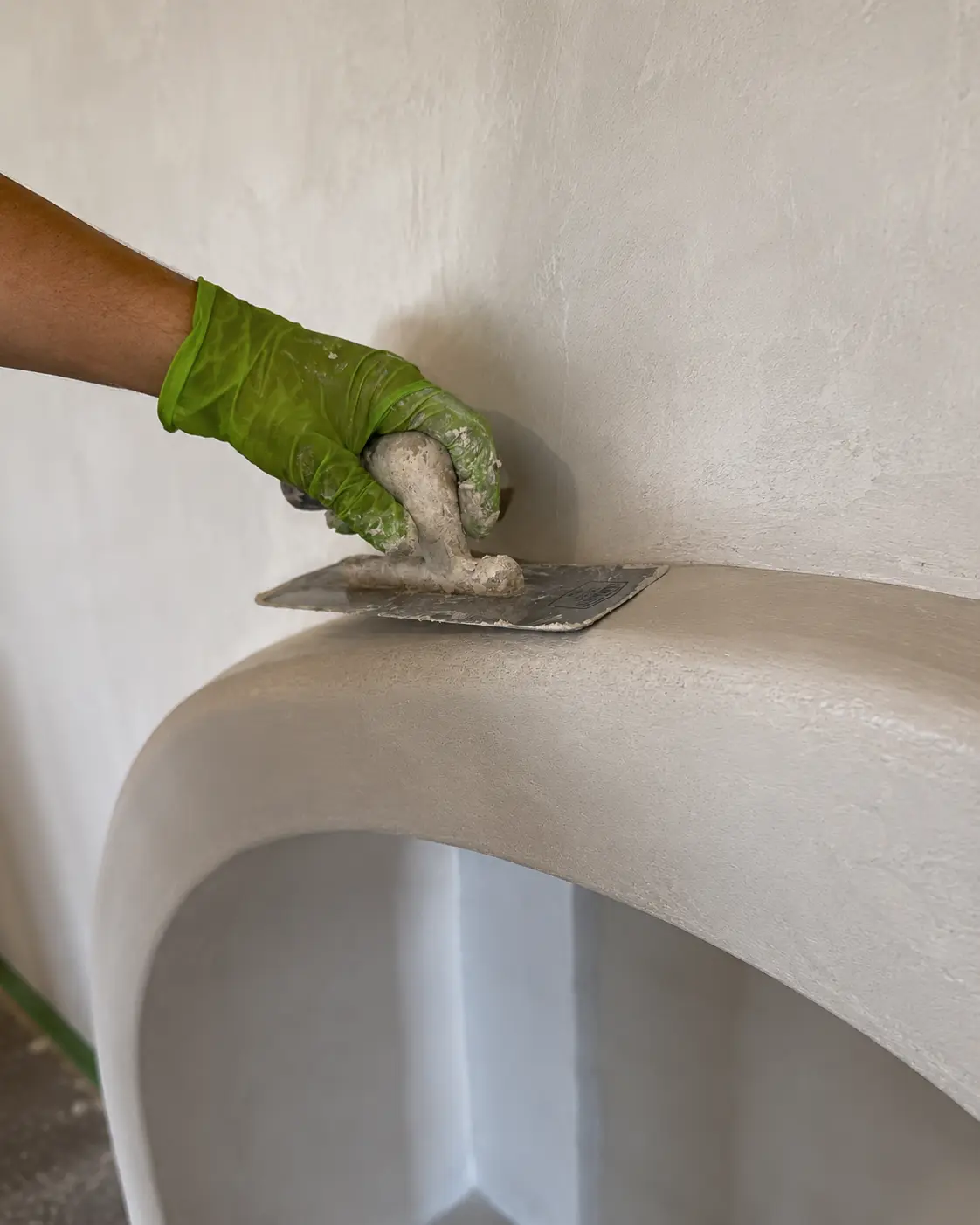 Specialist master hand-troweling the curved edge of the hearth to a smooth microcement finish.