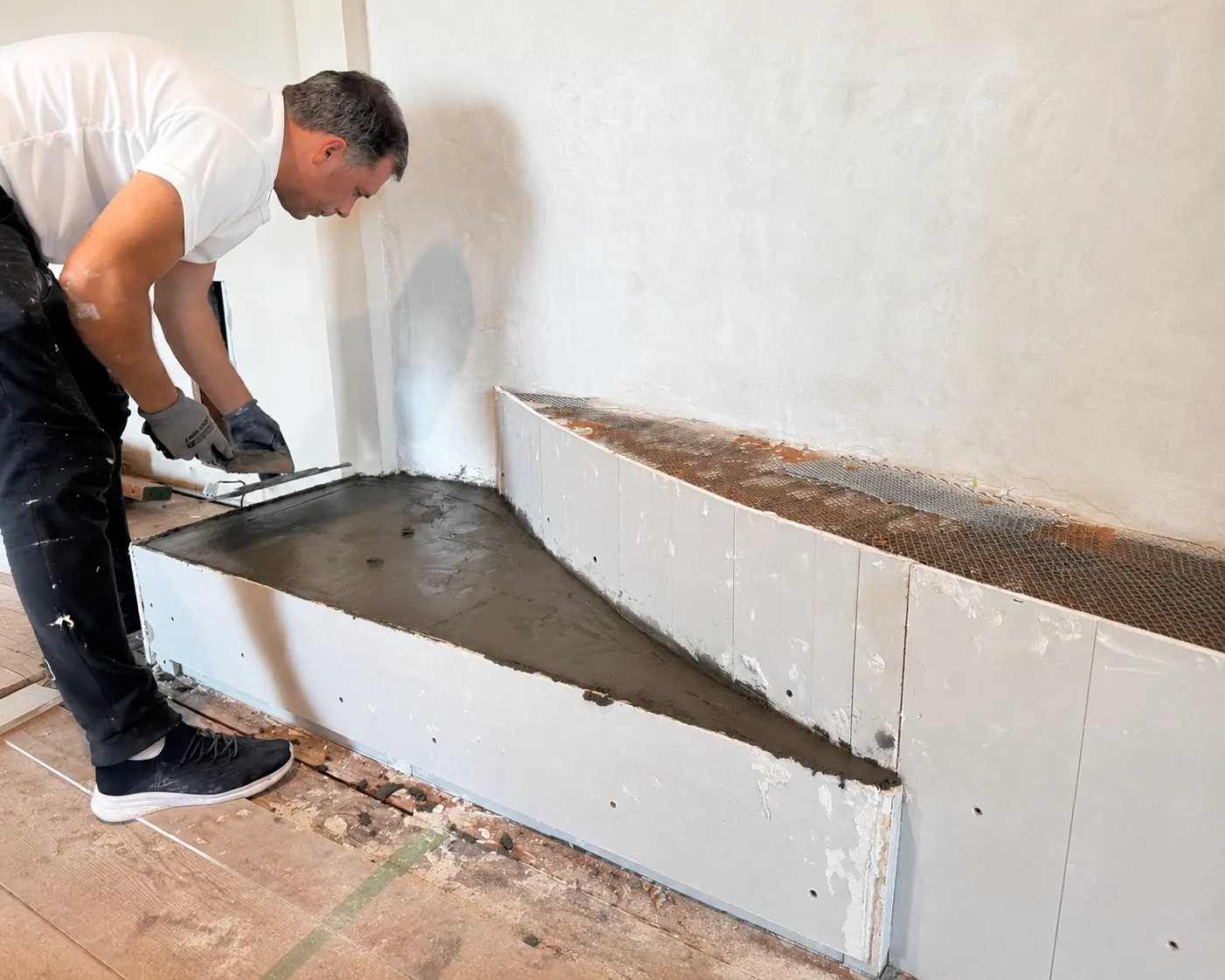 Specialist master applying cement mortar to the rebuilt lower hearth platform with metal mesh reinforcement.