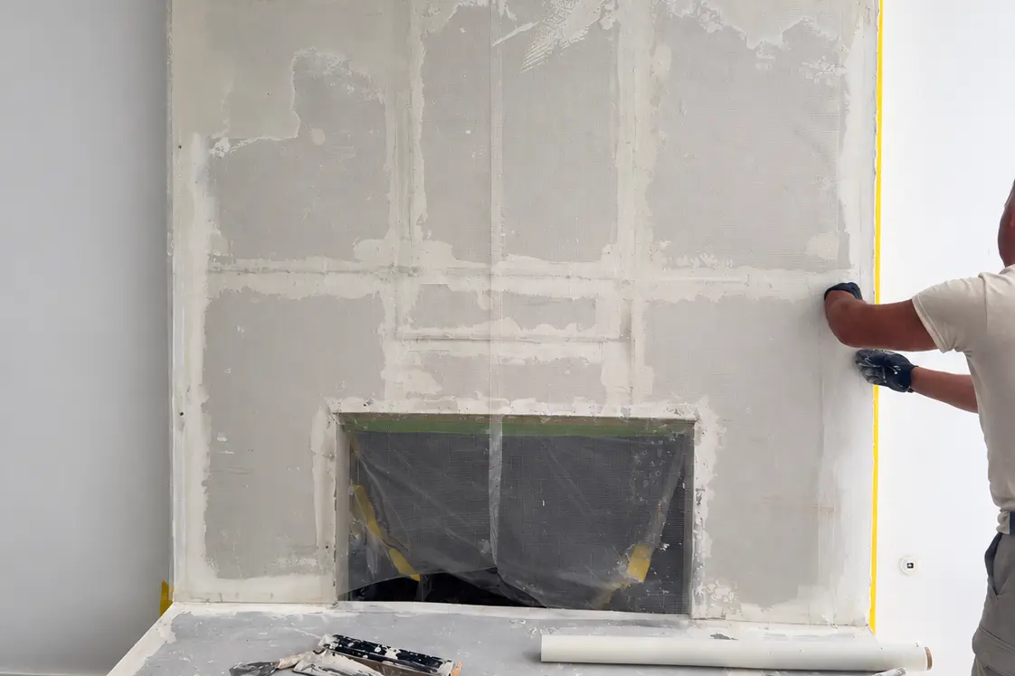 Specialist skimming leveling plaster across the fireplace chimney breast to a smooth continuous plane.