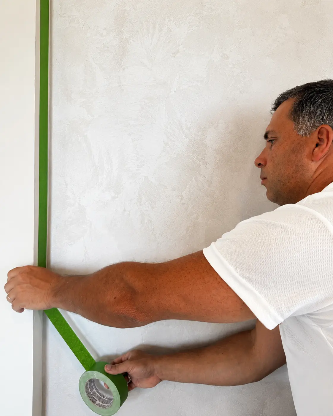 Specialist master taping green masking along a wall edge before microcement finishing.