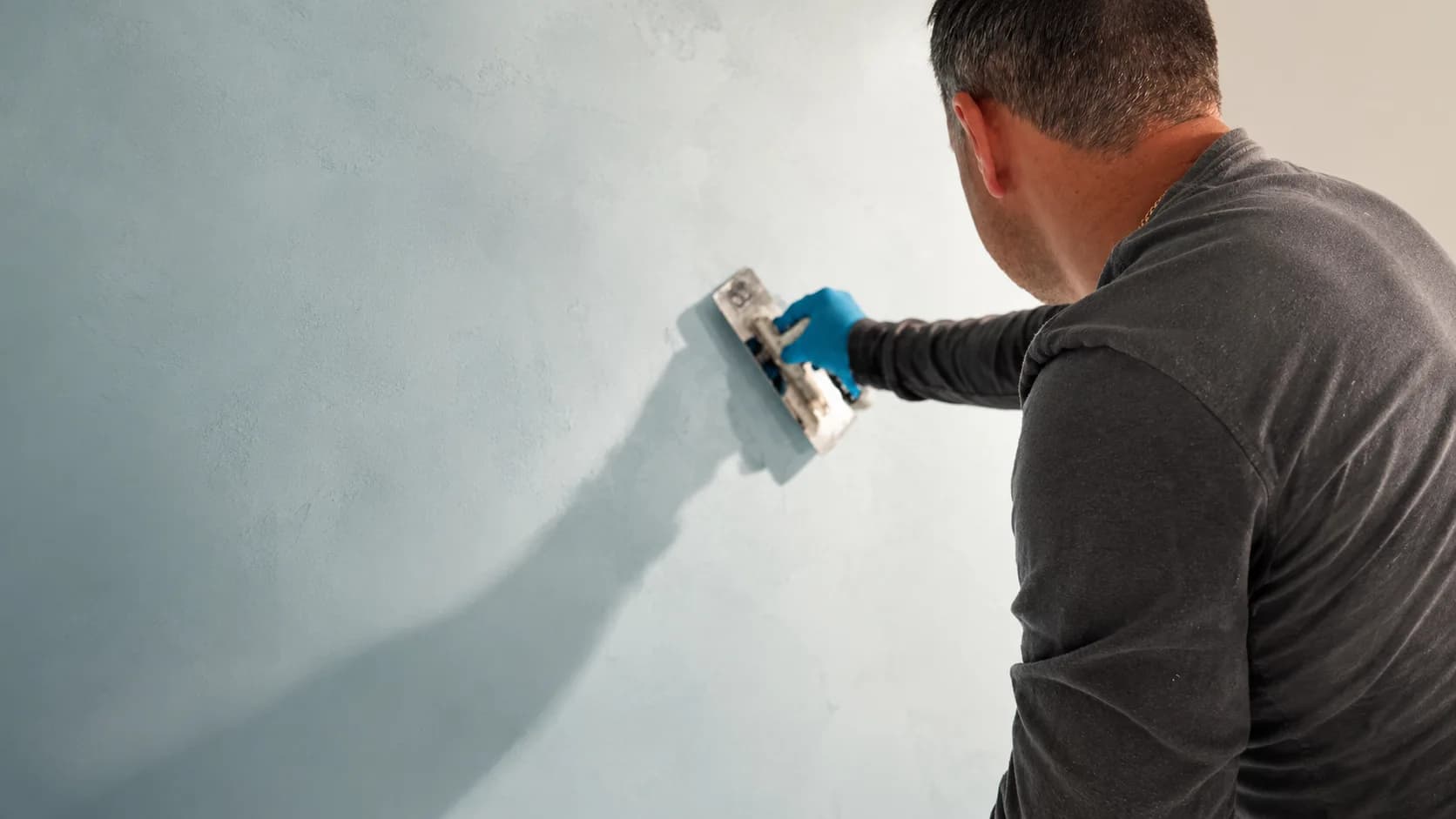 A finish specialist applying pale grey microcement to a wall with a steel trowel