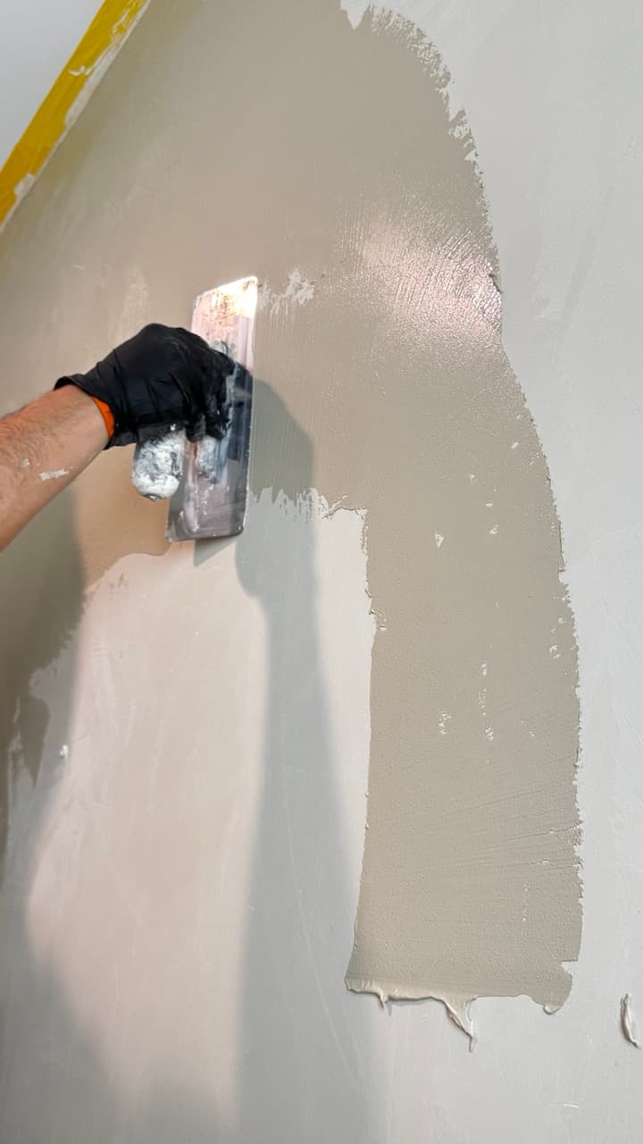 Close view of a trowel drawing the first coat of Marmorino Venetian plaster across a wall.