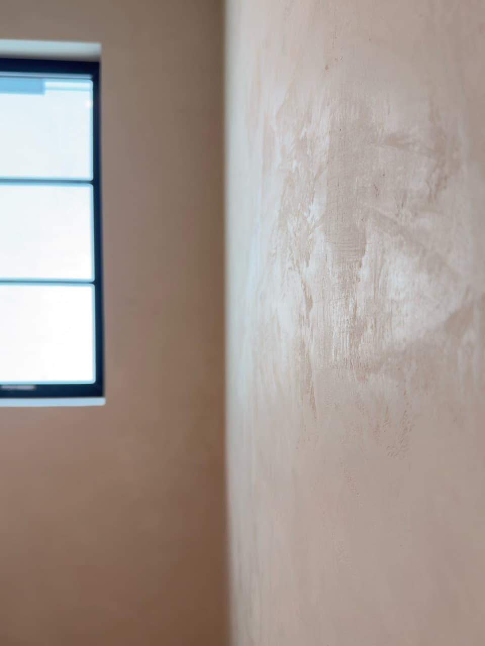 Close detail of matte Marmorino Venetian plaster texture in soft peach beside a window.