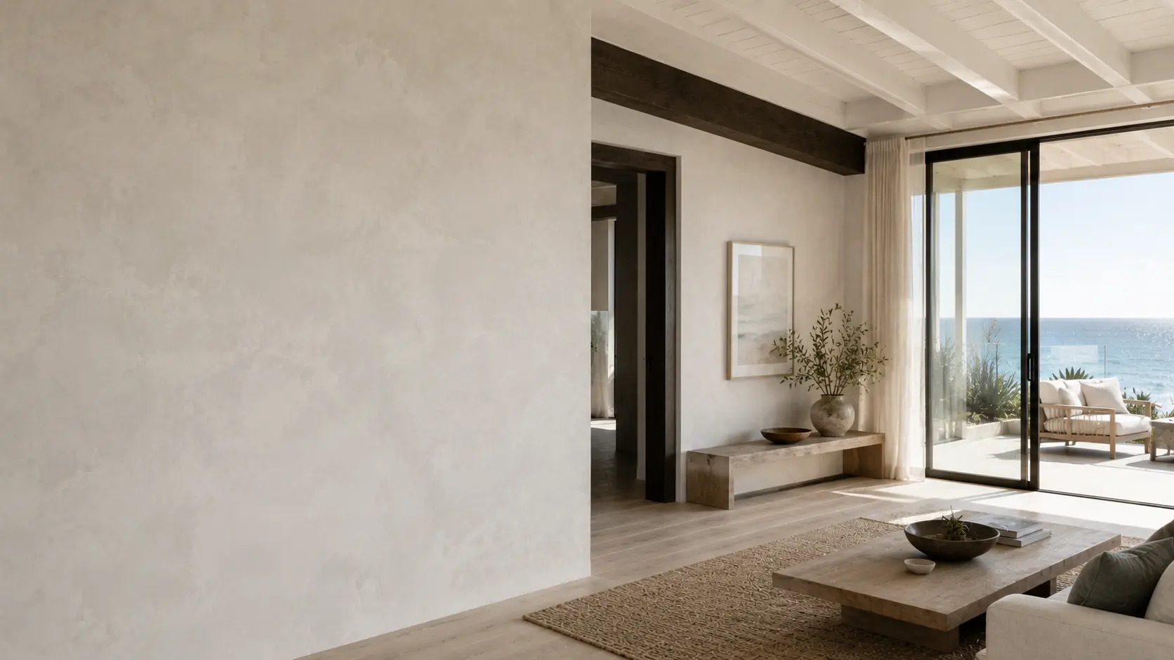 Coastal living room with lime wash walls opening onto an ocean view through glass doors